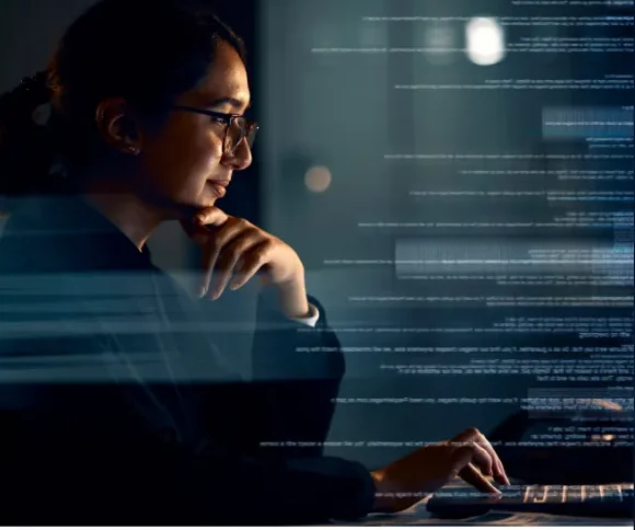 Woman with glasses at a computer at night behind an overlay of code
